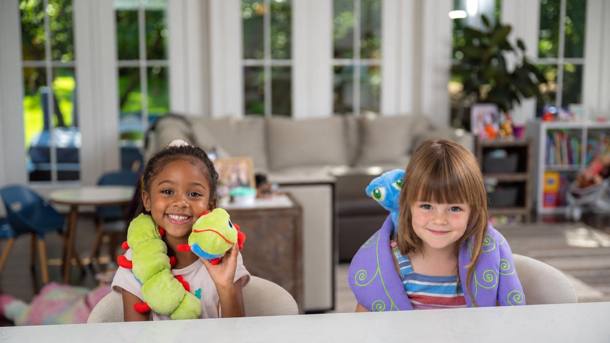 Two children in pyjamas on a family-room sofa in the evening, one holding Flutter.