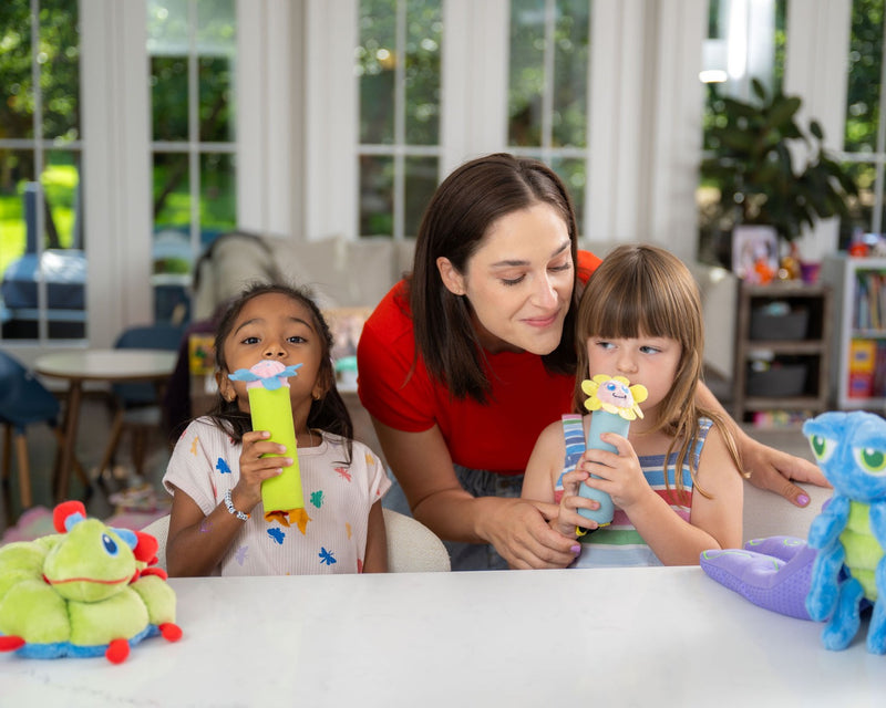 Two children at a table blowing through their Bloomie breathing sticks