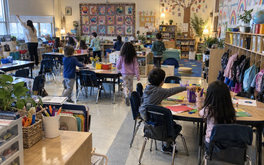 A busy primary classroom photographed from the back of the room, no faces visible.
